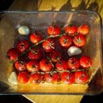 Geroosterde tomaten en knoflook op bakplaat in kamado of BBQ oven met kruiden en olie