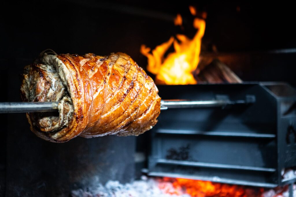 Gegrilde vleespen boven open vuur op kamado barbecue met vlammen op achtergrond