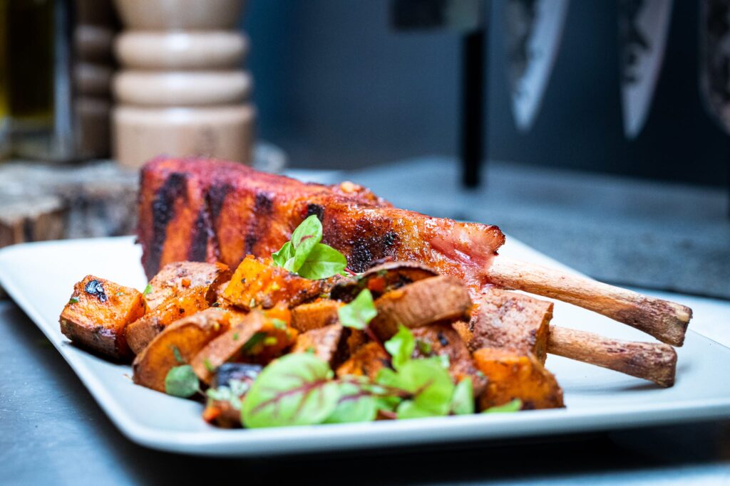 Gegrilde varkensribs met zoete aardappel en verse kruiden op witte bord, kamado BBQ gerecht