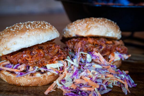 Twee pulled pork burgers op sesambroodjes met paarse koolsla op houten ondergrond.